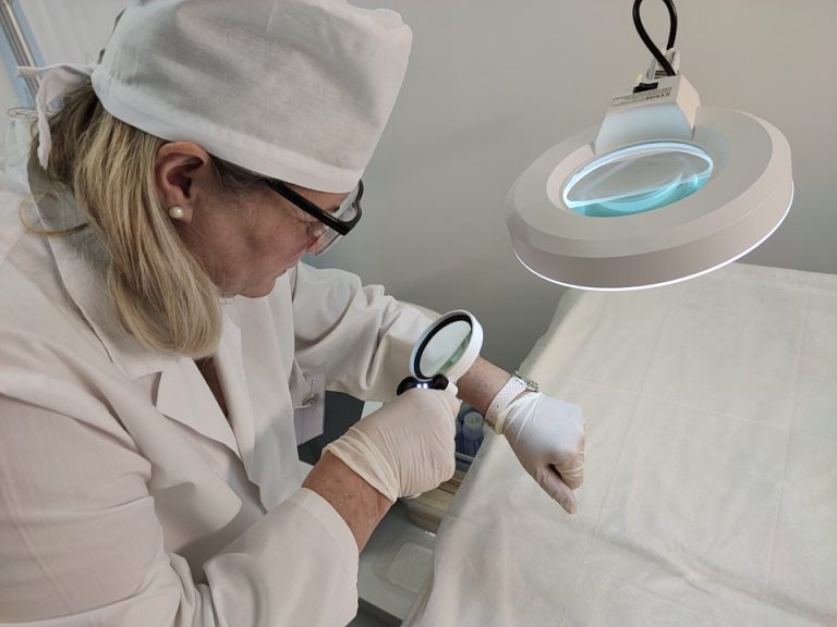 Un'operatrice esamina la pelle con una lente d'ingrandimento durante il check-up prima del laser